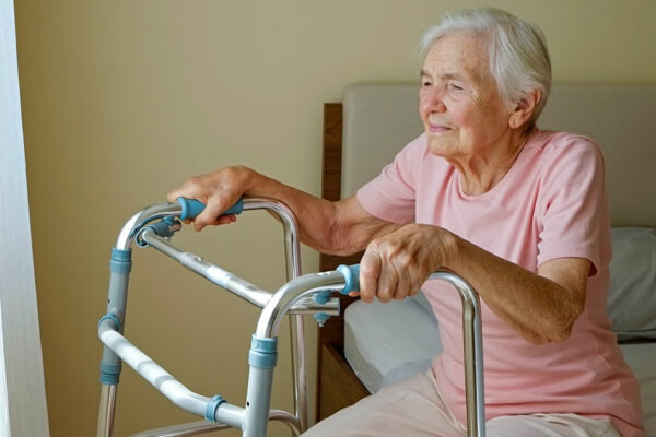 Seniorin sitzt auf einem Bett und hält sich am Rollator fest | Umzug ins Pflegeheim