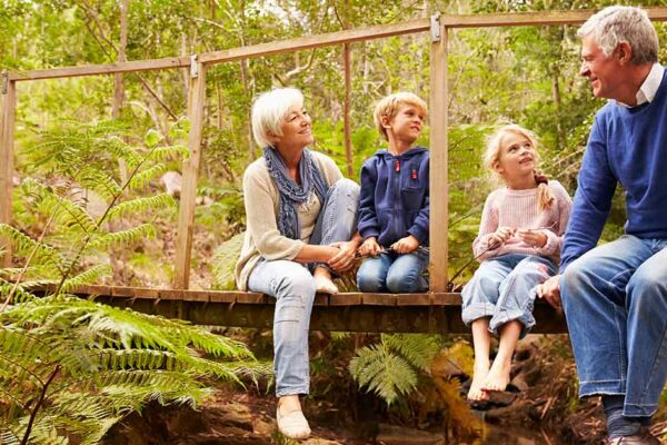 Großeltern sitzen mit Enkeln auf einer Holzbrücke im Wald - Wohnen im Alter