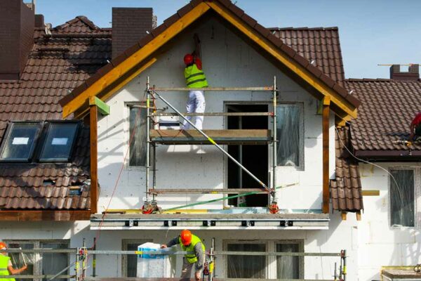 Mehrere Handwerker stehen auf einem Gerüst an einem Haus und arbeiten | Immobilie modernisieren sanieren