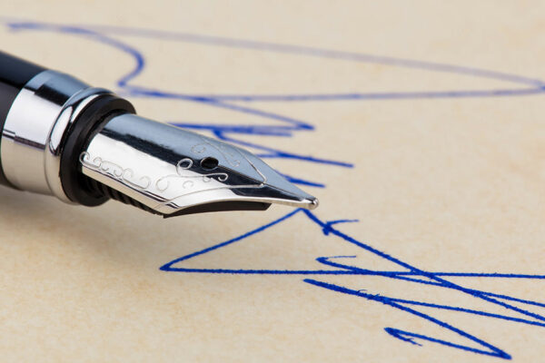 Eleganter Füller, mit dem mit blauer Tinte eine Unterschrift geschrieben wird | Kaufpreiszahlung nach Notartermin